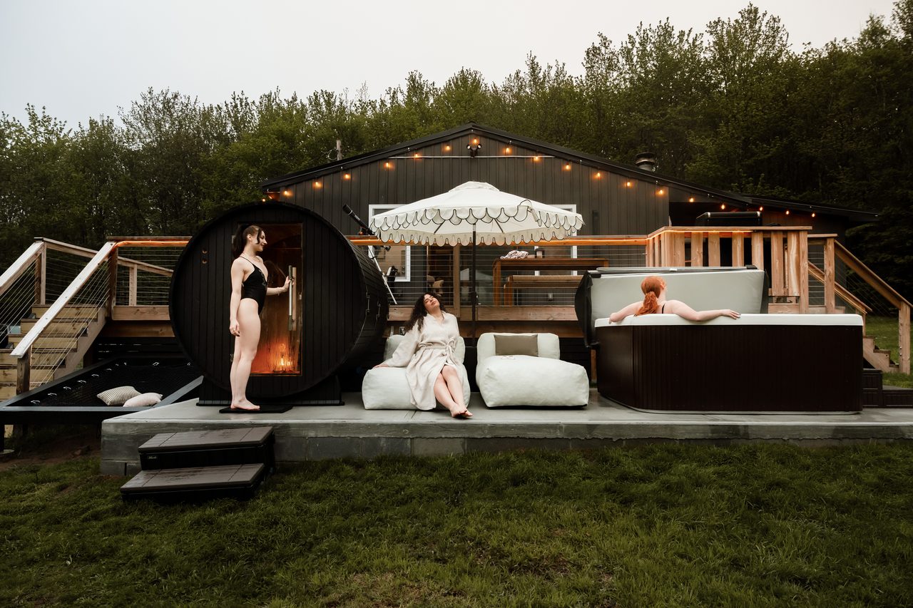 Guests at the barrel sauna and hot tub on the deck at dusk, Catskills cabin with a hot tub and sauna