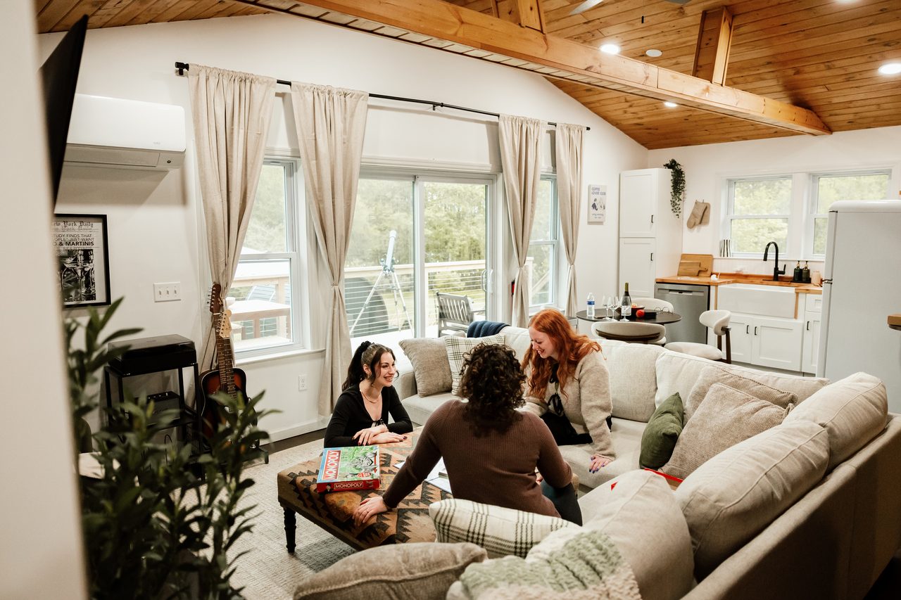 Three friends gathered around the sofa in the open great room of a Catskills cabin that sleeps 8, Livingston Manor NY
