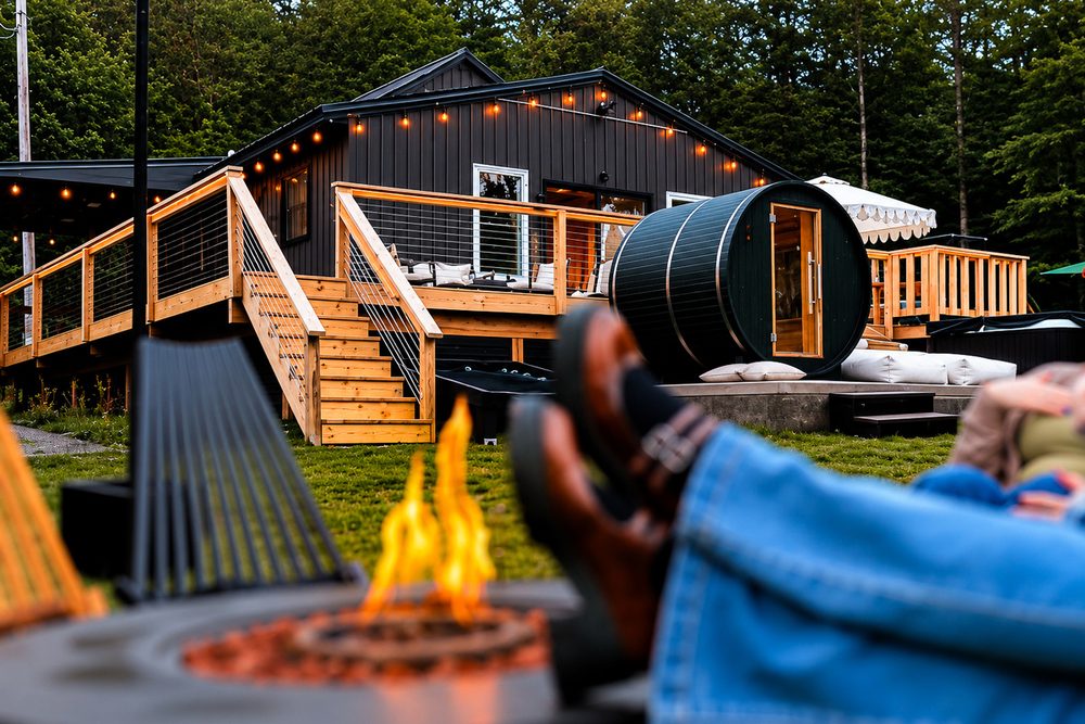 Evening at the fire pit with outdoor lounge seating, string lights and the barrel sauna behind