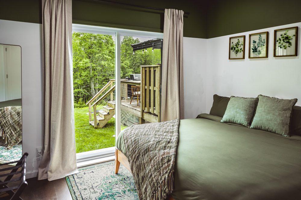 The Sunrise Suite: king bedroom with glass doors opening to the woods and forest-green bedding