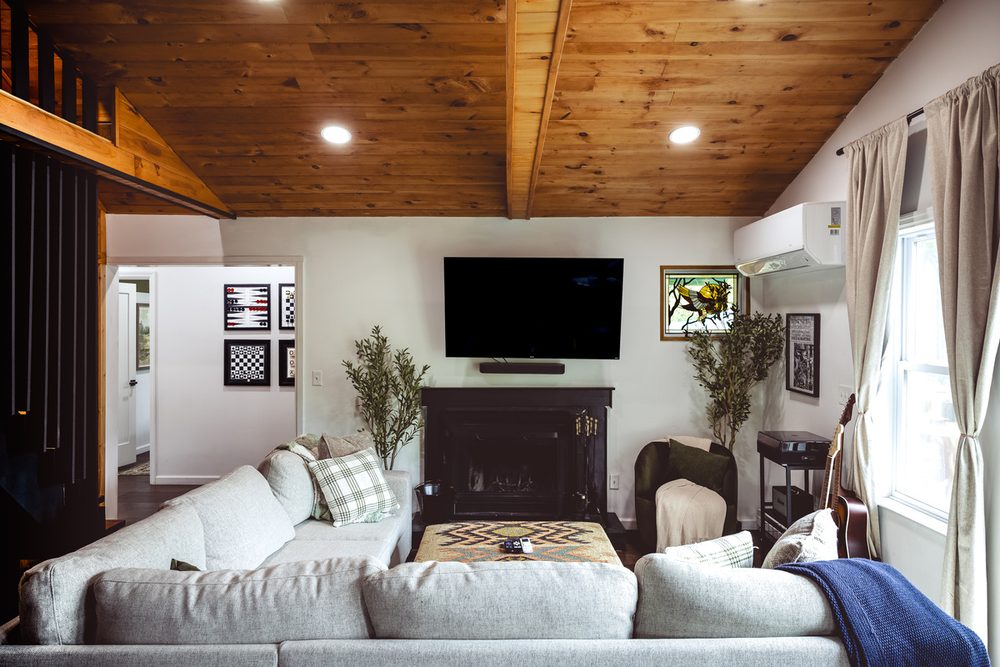 Living room with a vaulted wood ceiling, fireplace, large smart TV, sectional and houseplants