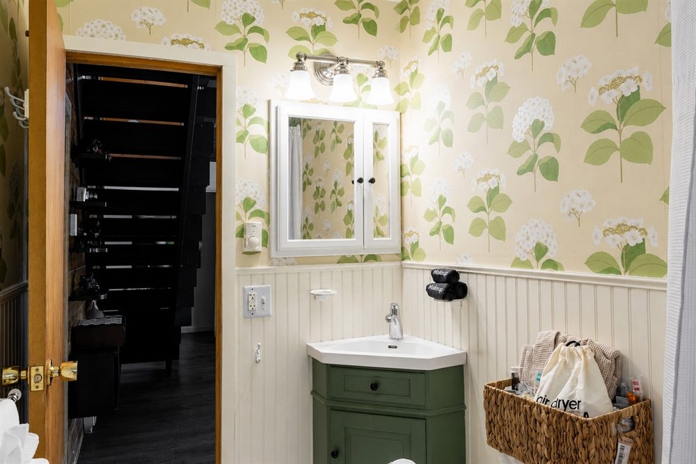 Bathroom with botanical wallpaper, beadboard and a green vanity