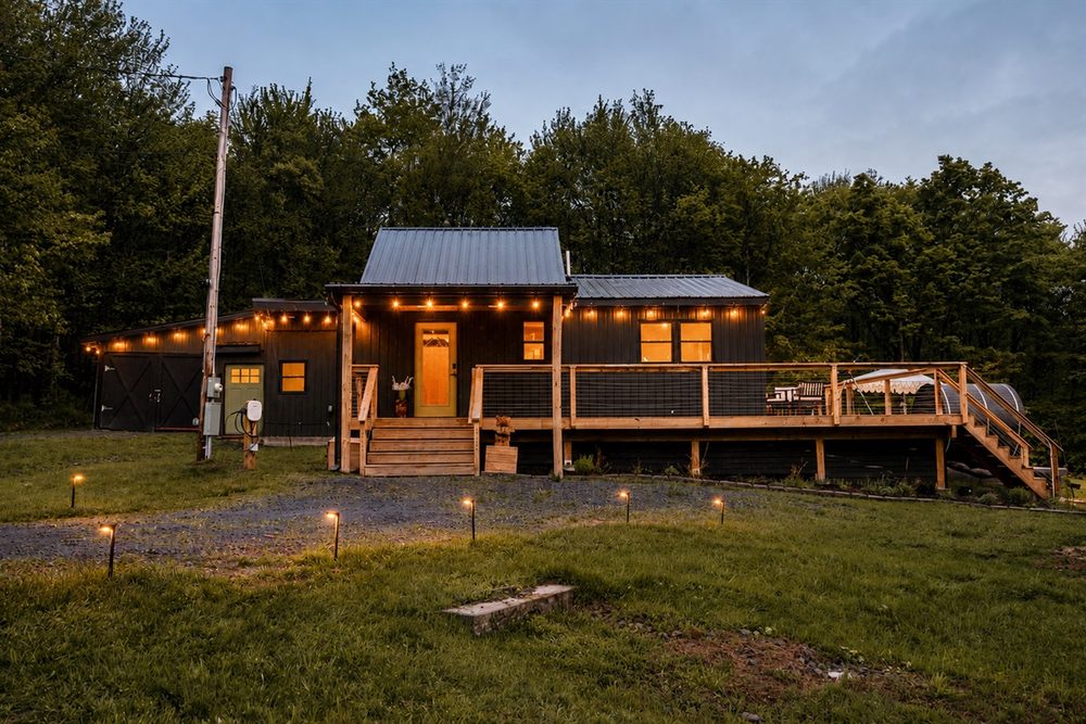 The cabin and deck at dusk, lit with string lights against the dark forest