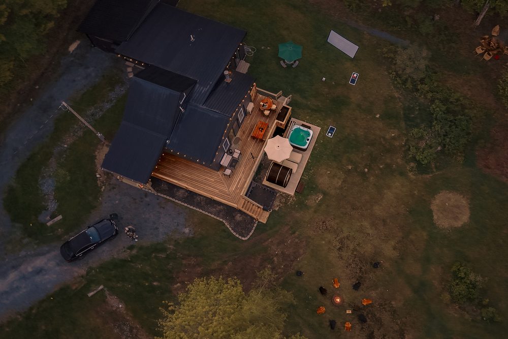 Top-down aerial view of the cabin roof, deck, hot tub and fire pit clearing