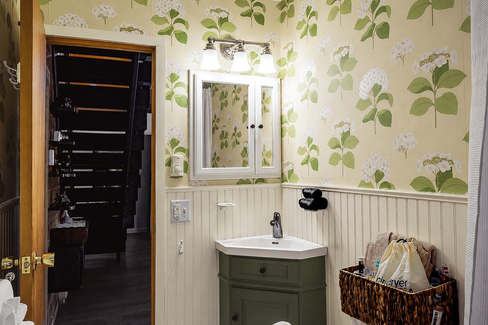 Botanical-wallpaper bathroom with a white vanity mirror and green cabinet