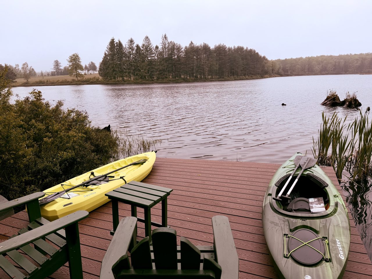 Two kayaks with paddles and Adirondack chairs on the private dock at the misty lake, a short walk from the cabin near Livingston Manor, NY