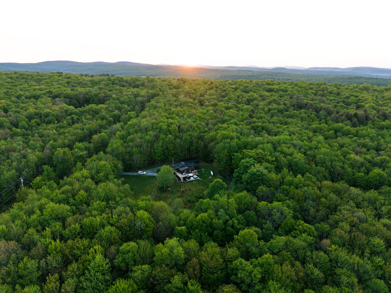 Aerial view of the cabin alone in a vast Catskills forest with mountains at sunset, a secluded retreat on wooded acres near Livingston Manor, NY
